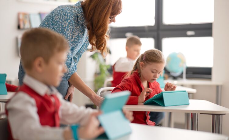 Schoolgirl with down syndrome using digital tablet during lesson in classroom at primary school.